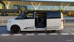 Wypożyczalnia Samochodów Edition Cars prezentuje Multivana T7 dostępnego w gdańsk w środku od boku na tle lotniska W gdańsku
